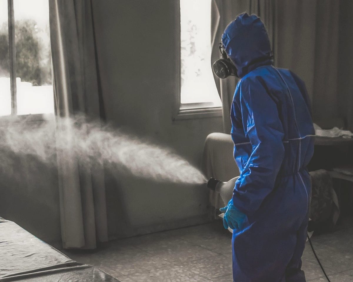 Técnico com traje de proteção e máscara facial aplicando nebulização dentro de um imóvel